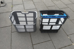 Zwei Filterkörbe in Grau und Schwarz stehen nebeneinander auf Steinboden. Beide bestehen aus Kunststoffgittern mit eingespannten Filtermembranen und blauen Haltegriffen.