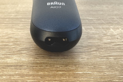 Der untere Teil eines Rasierers mit der Aufschrift „BRAUN AIO7“ ist zu sehen. Im Fokus steht der doppelte Ladeanschluss mit zwei runden Kontakten.