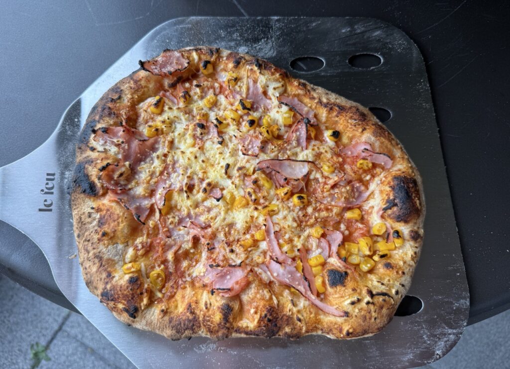 Frisch gebackene Pizza mit Schinken, Mais und Käse auf Pizzaschieber aus Metall.