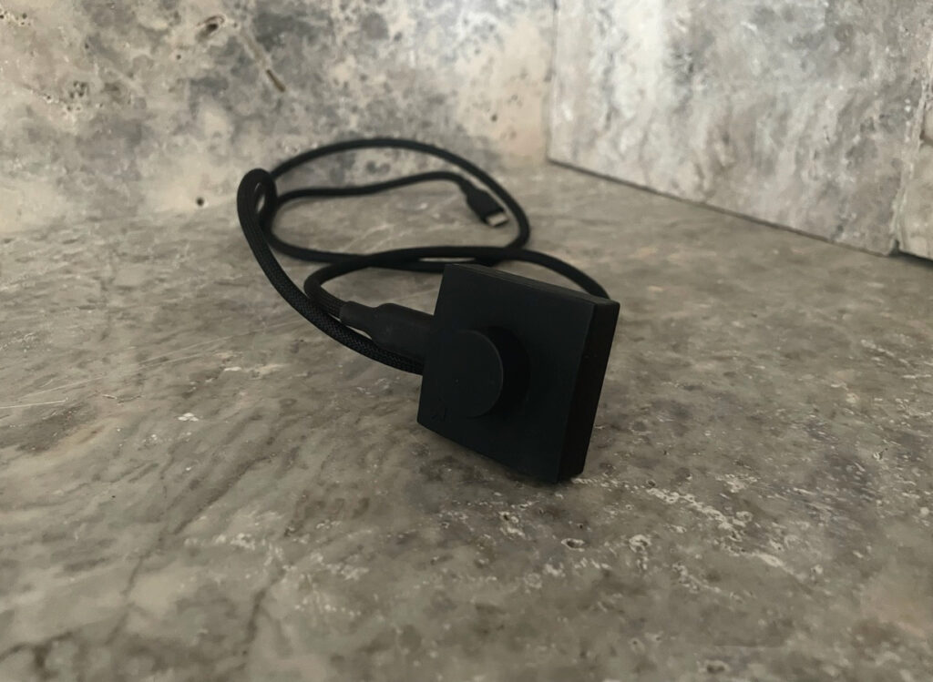 Schwarzes USB-Ladekabel des UltraHuman Ring AIR mit quadratischer Ladevorrichtung.