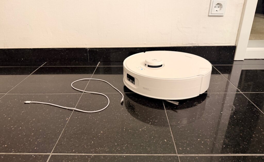 Roborock Qrevo Curv 2 Flow: Roboter neben einem Ladekabel auf Fliesenboden