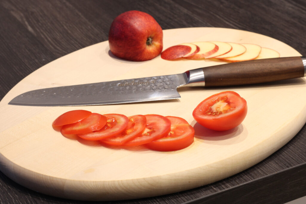 adelmayer Damastmesser Santokumesser 17,5 cm Gesamtansicht auf Schneidbrett mit geschnittener Tomate und geschnittenem Apfel